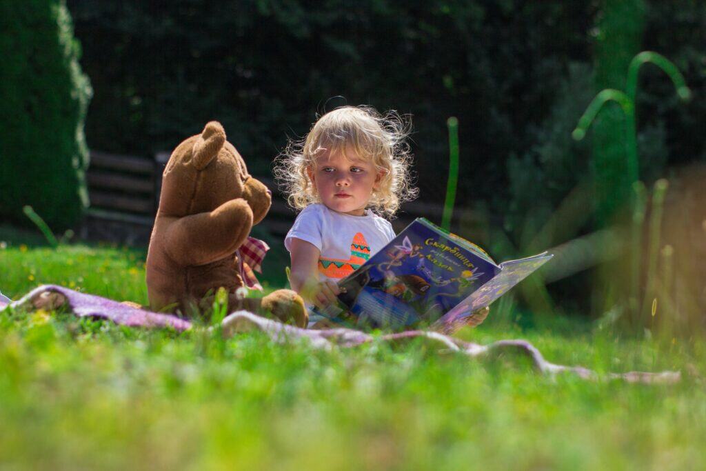 Kleinkind mit Bilderbuch und Kuscheltier im Garten – Symbolbild für Alltagssituationen im 1:1 Coaching für Eltern.
