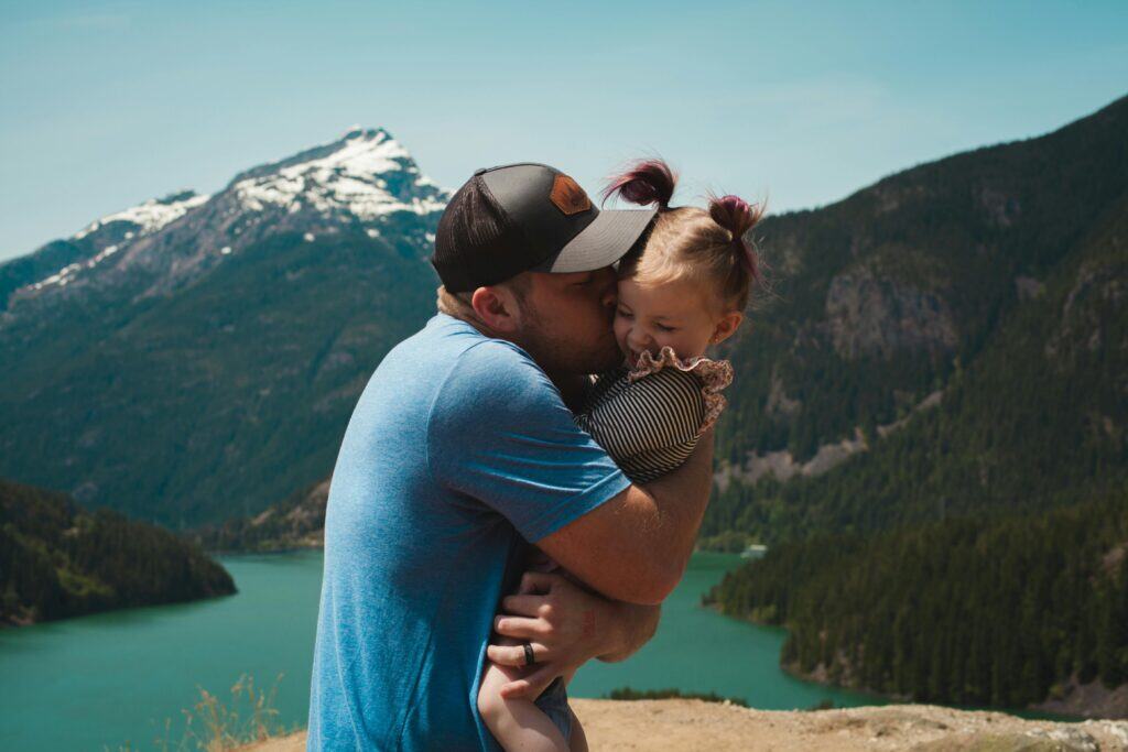 Vater küsst sein Kind innig vor Bergkulisse – 1:1 Coaching für Eltern unterstützt echte Verbindung im Familienalltag.