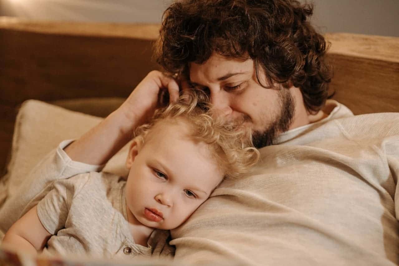 Vater liegt mit seinem Kind im Arm auf dem Sofa – Nähe und Geborgenheit als wichtiges Bedürfnis, KinderLiebe Blog.