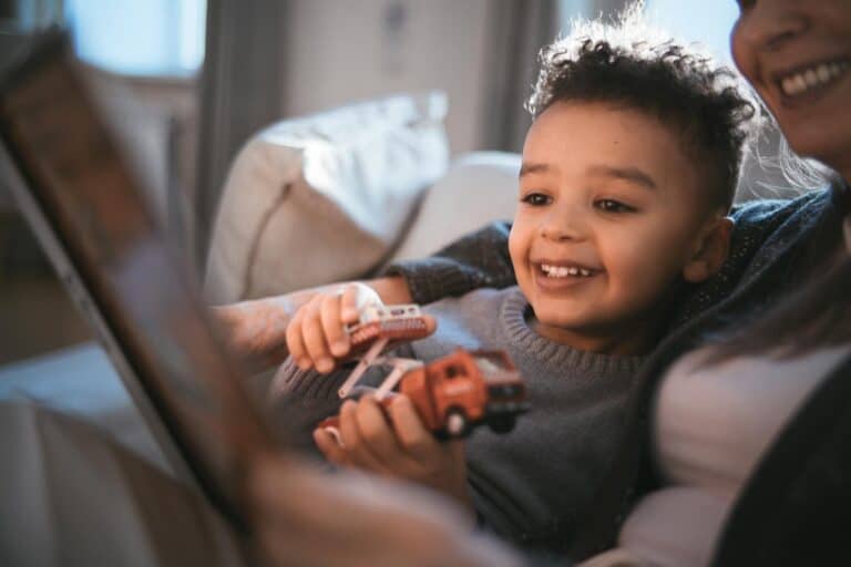Kind lächelt beim Anschauen eines Buches mit Spielzeugauto in der Hand im Arm eines Elternteils. KinderLiebe Coaching unterstützt Eltern dabei, das Verhalten und die Bedürfnisse ihrer Kinder besser zu verstehen.