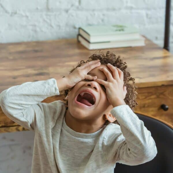 Emotional überfordertes Kind hält sich die Hände vors Gesicht. Starke Gefühle im Familienalltag