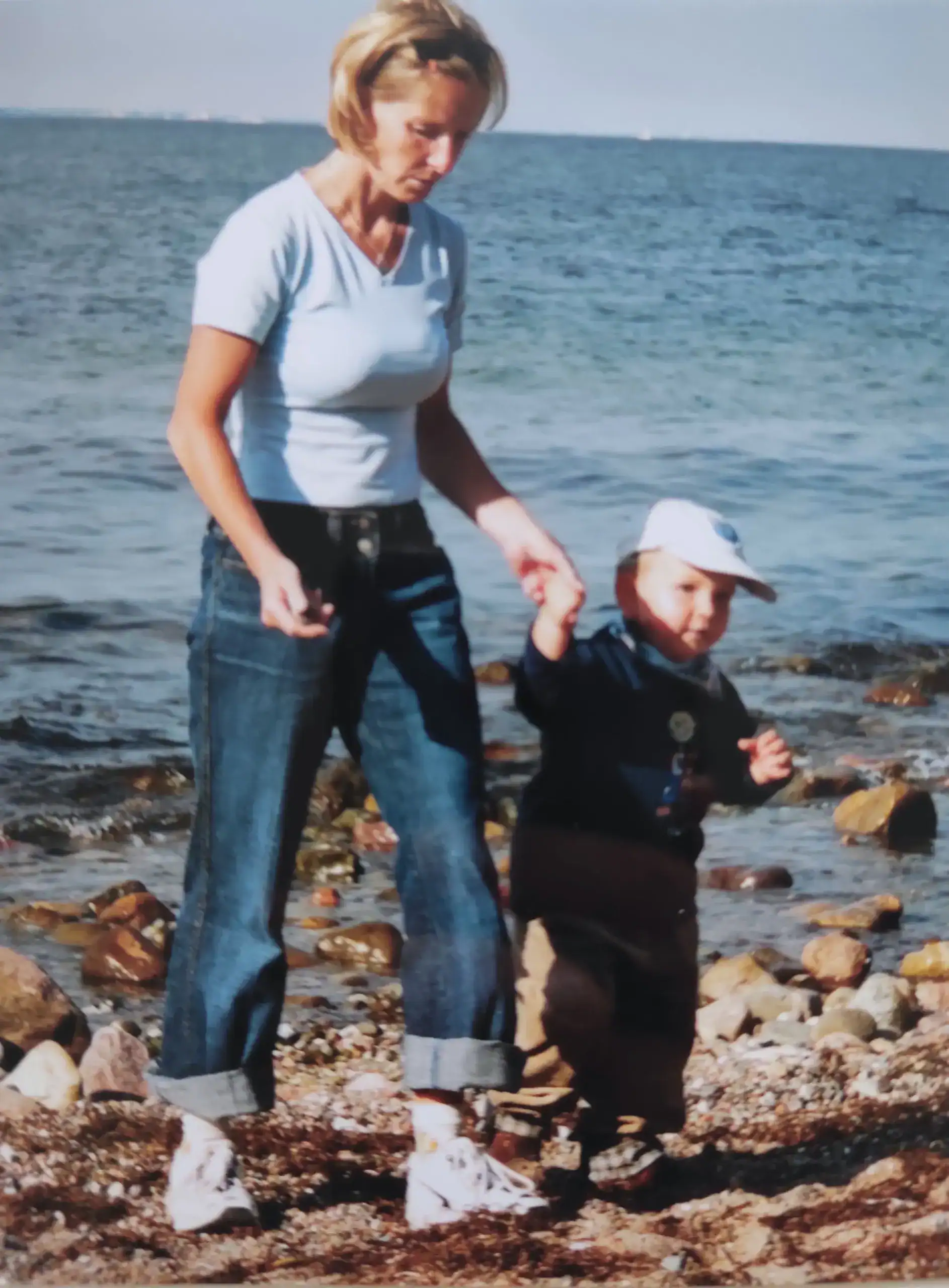 Daniela Bernauer mit ihrem Kleinkind am steinigen Strand – Mutter hält die Hand ihres Sohnes beim Spaziergang.
