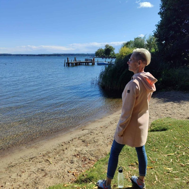 Daniela Bernauer am Seeufer. Elterncoach blickt nachdenklich und kraftvoll in die Weite, Offenheit für Veränderung.