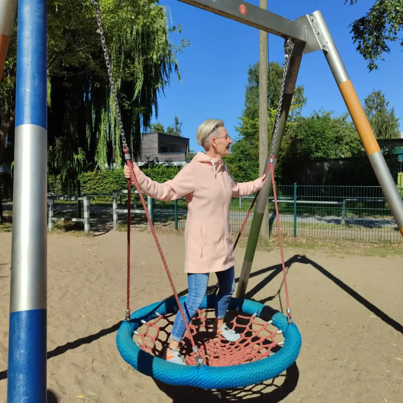 Daniela Bernauer lacht auf einer Nestschaukel am Spielplatz – Elterncoach zeigt natürliche Lebensfreude und Leichtigkeit.