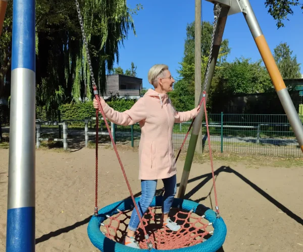Daniela Bernauer lacht auf einer Nestschaukel am Spielplatz – Elterncoach zeigt natürliche Lebensfreude und Leichtigkeit.