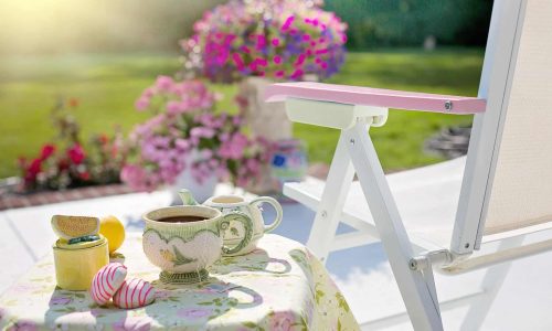 eltern-selbstfuersorge-kinderliebe-blog Tasse Tee und Teekanne auf einem Gartentisch in der Sonne – ein Moment der Ruhe und Selbstfürsorge für Eltern, KinderLiebe Blog.