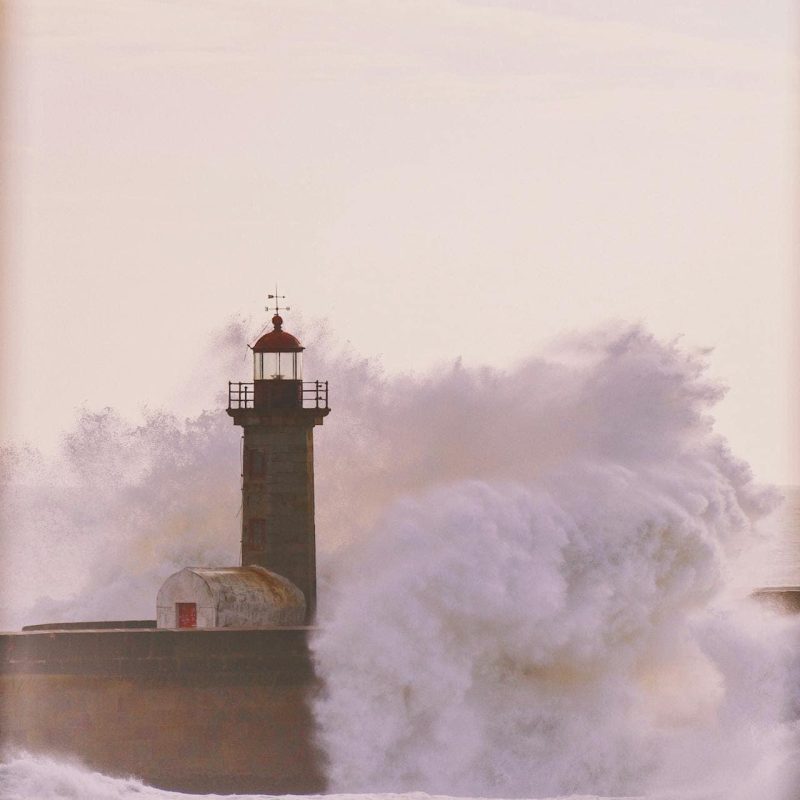 Ein Leuchtturm steht fest, während riesige Wellen gegen ihn schlagen.